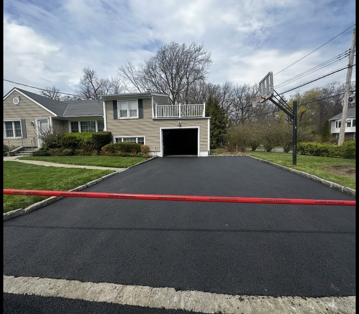 The same driveway after the work: a smooth, fresh black asphalt surface laid up to the granite cobble apron